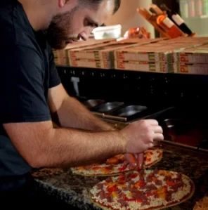 Le pizzaiolo de La Bri'Antine garnit une pizza