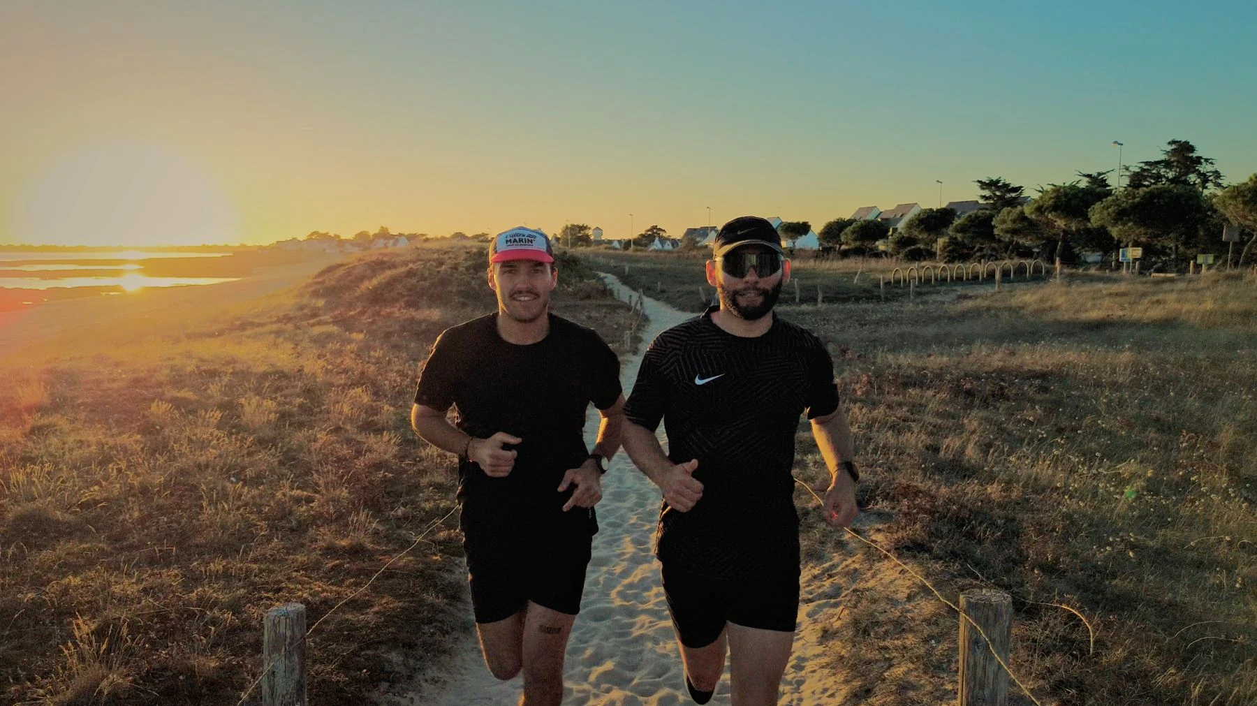 Deux coureurs souriants sur le sentier de sable au coucher du soleil